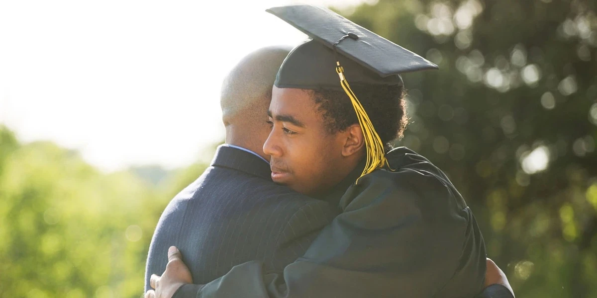 A student in a graduation cap and gown hugs a family member